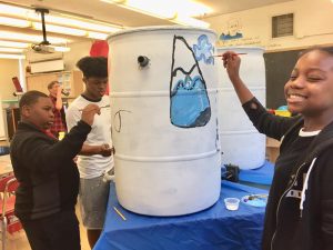Three boys paint a rain barrel.